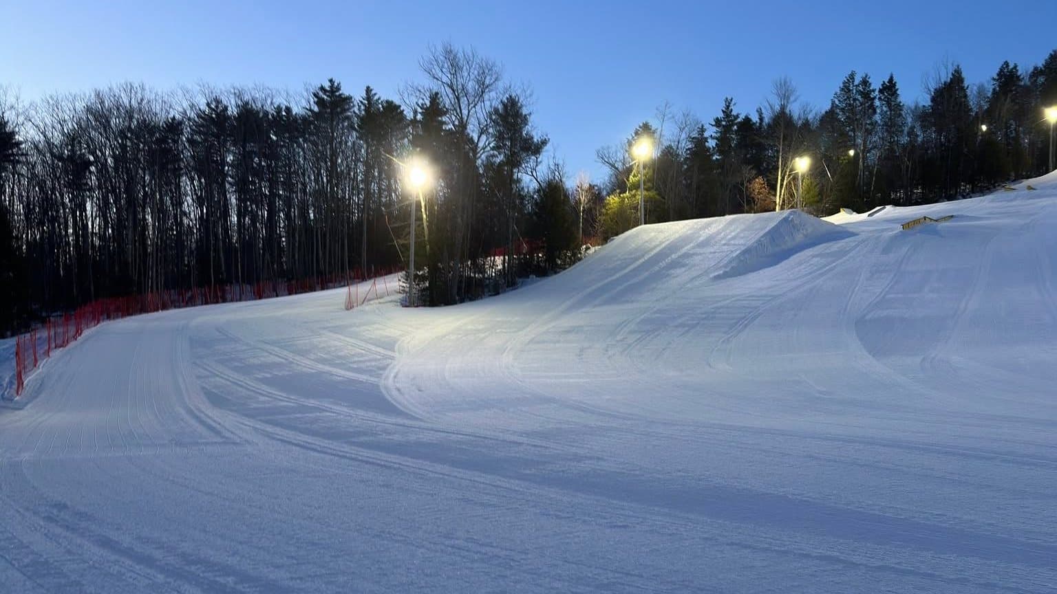 The main slope at Abenaki groomed and lit at dusk, lights on along the treeline