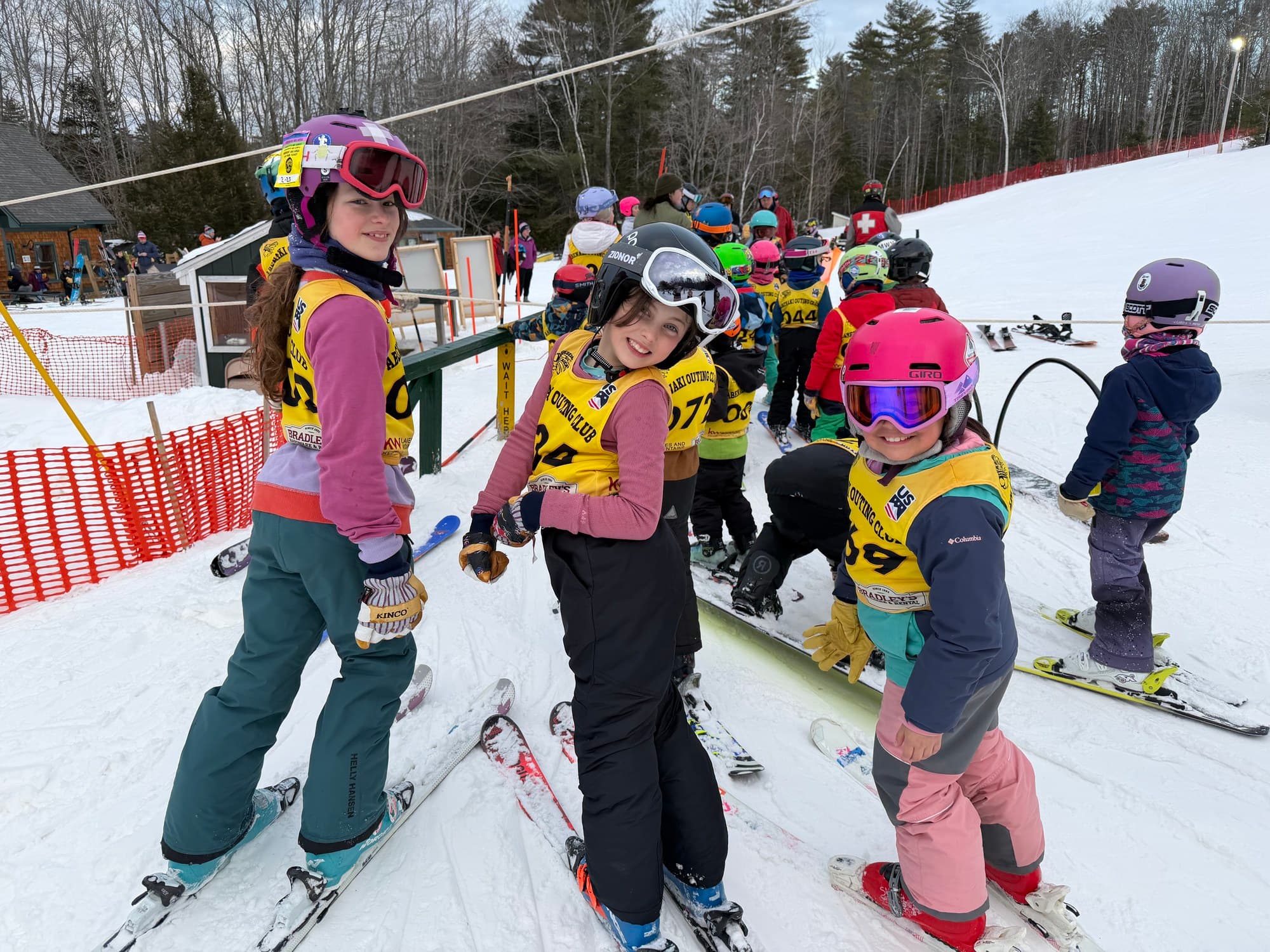 Three U10 racers in Abenaki Outing Club bibs at the start line, teammates lining up behind them
