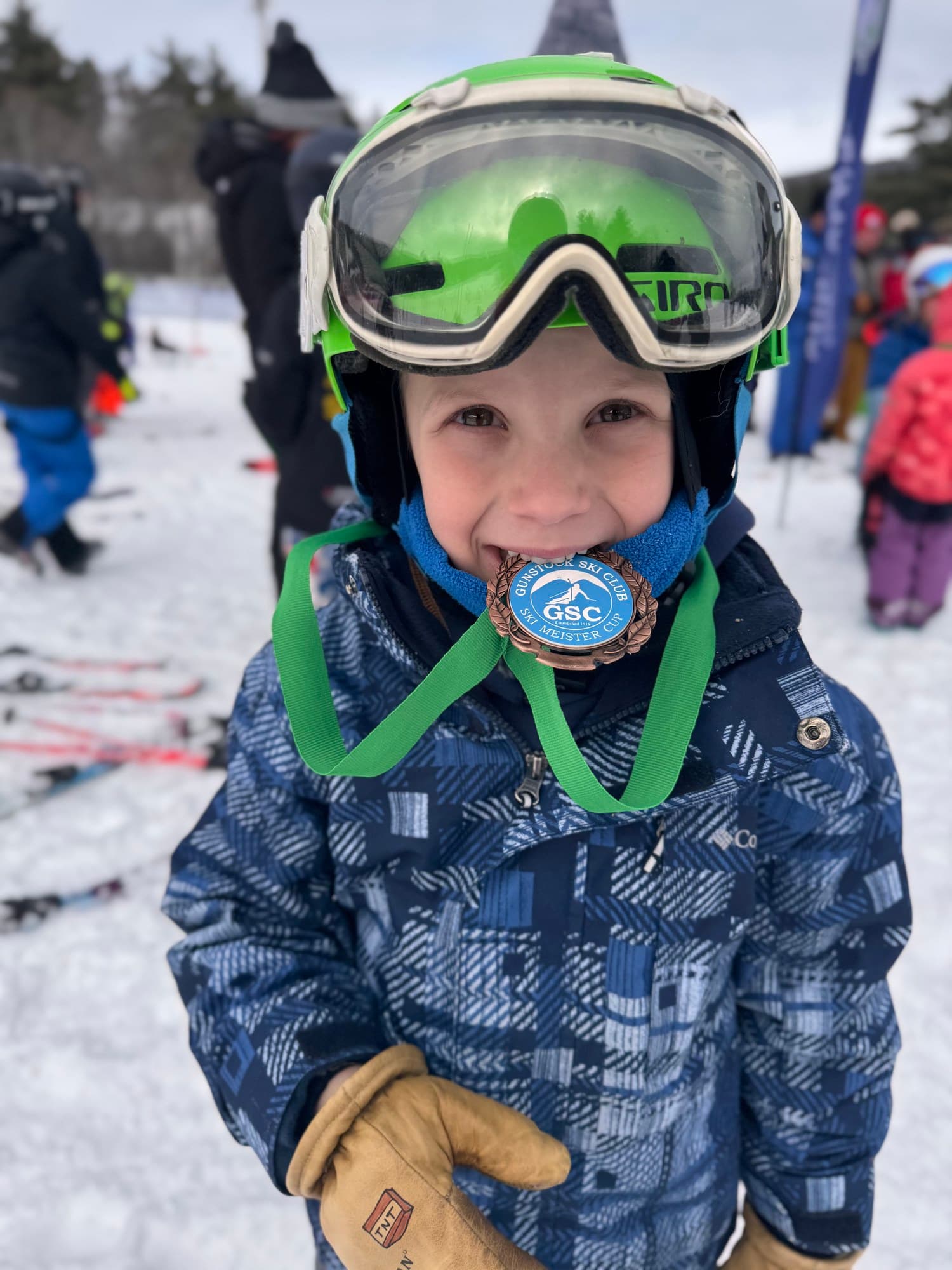 A U8 racer in a green helmet biting the medal from a Gunstock race